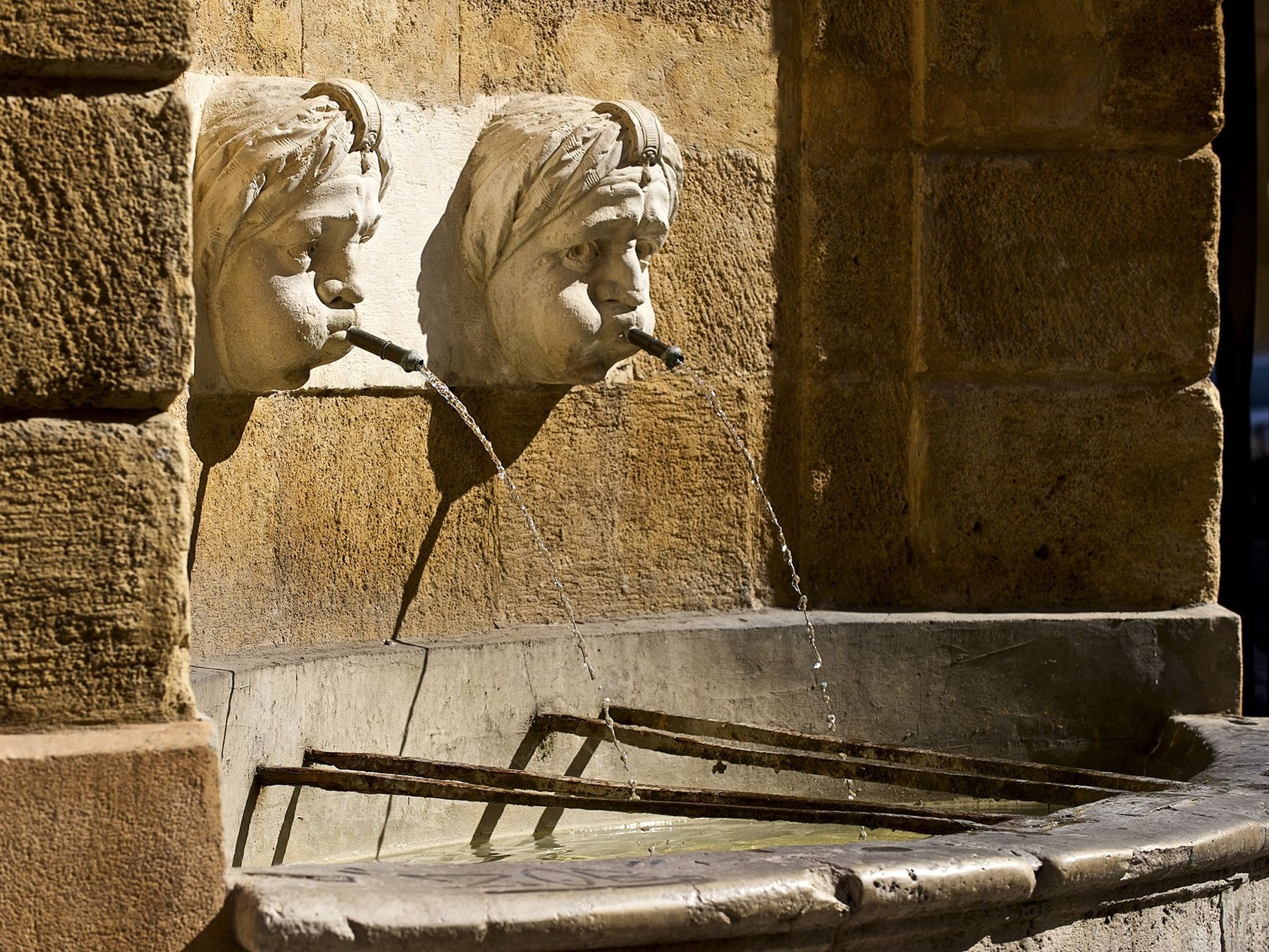 Deux mascarons de pierre crachent l'eau d'une fontaine d'Aix